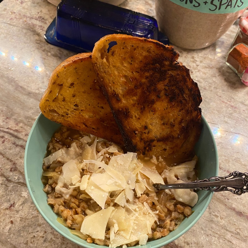 A bowl of cabbage and farro soup, topped with shaved parmesan, with two slices of grilled bread.